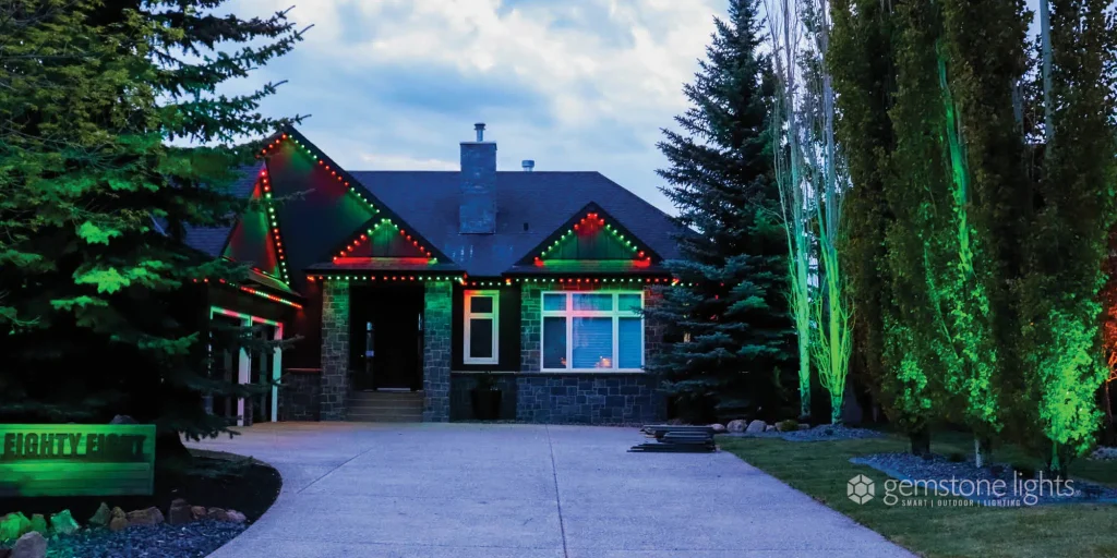 Outdoor lighting installation in Heights Billings illuminates a house with vibrant red and green lights among lush trees