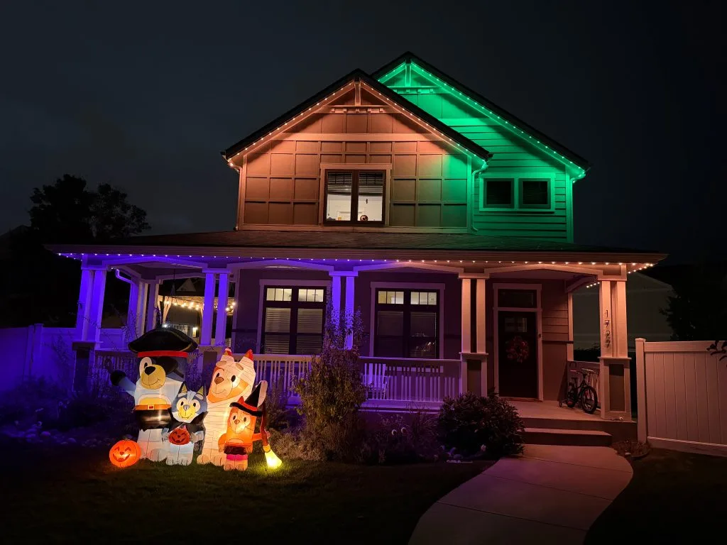 A house is brightly lit with colorful Halloween decorations and inflatables