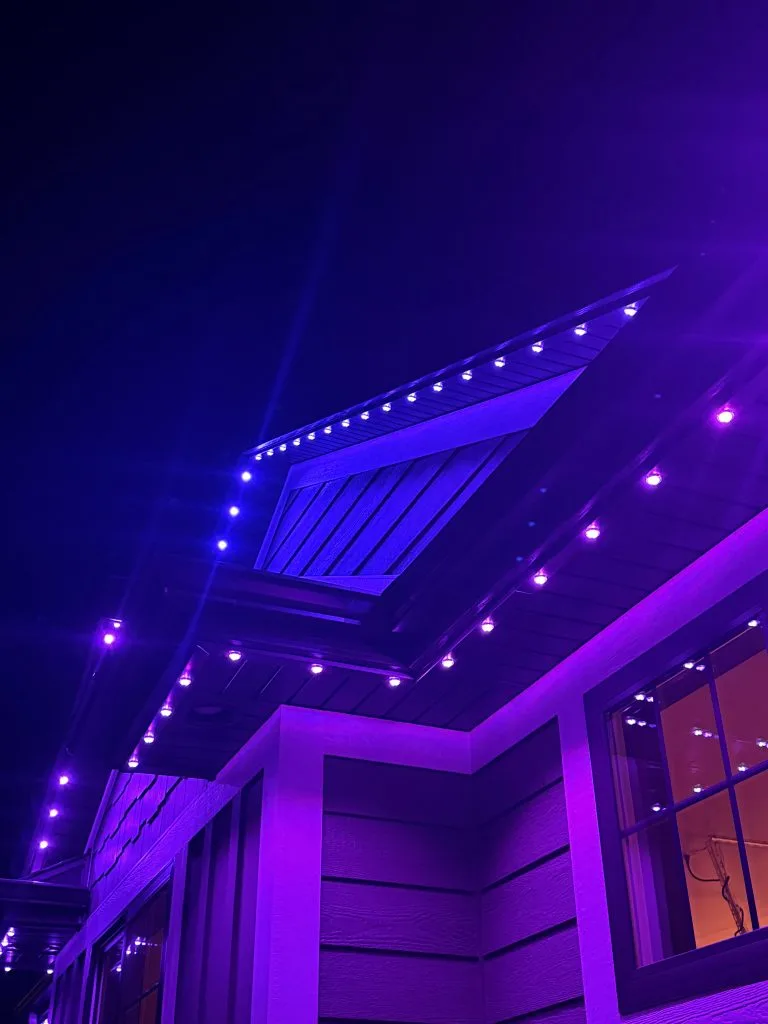 Vibrant purple lights illuminate the edges of a house against the night sky