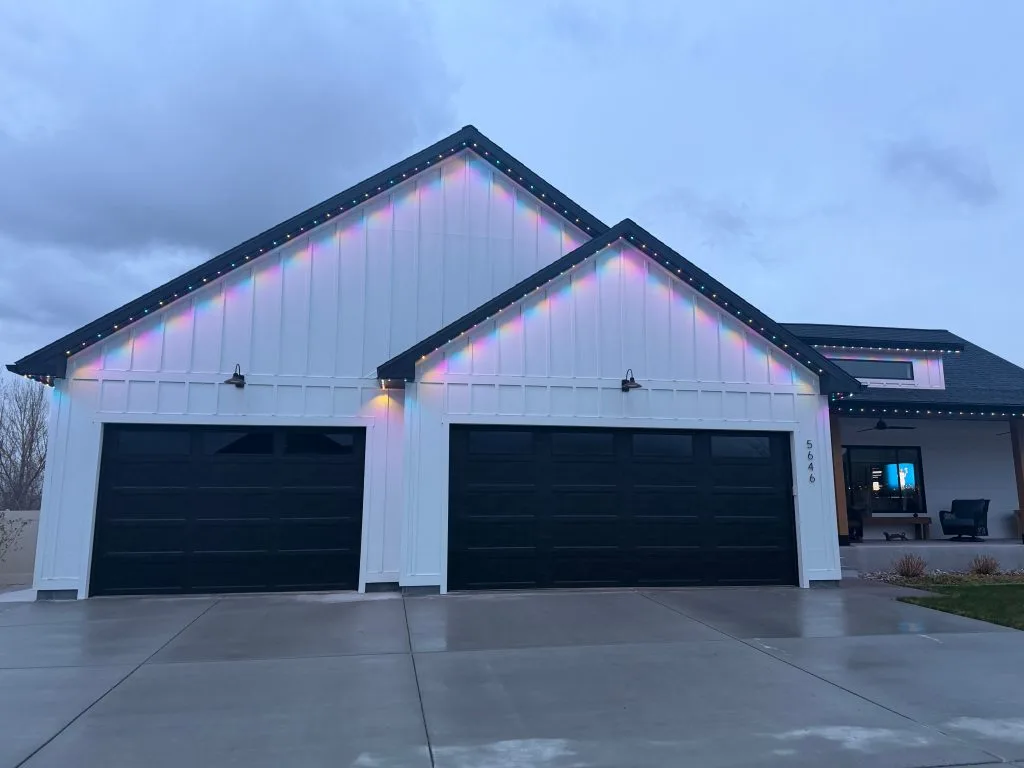 A modern house features black garage doors and colorful lights along the roof